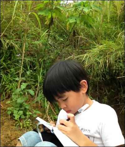 Kaaro writing and sketching on his book while resting on the trail.